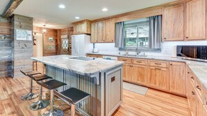 A modern kitchen with wooden cabinets, a large island with bar stools, and a built-in oven. - On Lake Tillery: Spacious Home w/ Screened Porch! (Albemarle)