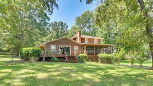 A two-story wooden house with a porch, surrounded by a well-maintained lawn and trees. - On Lake Tillery: Spacious Home w/ Screened Porch! (Albemarle)