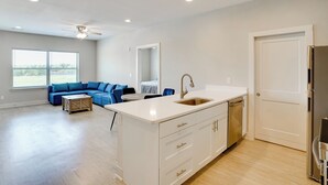A modern kitchen with a white island, stainless steel appliances, and a blue sofa in the living area. - Gateway to Fort Worth & Burleson! Couples Apt (Crowley)