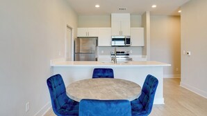 A modern kitchen with white cabinets, stainless steel appliances, and a central island with blue chairs. - Gateway to Fort Worth & Burleson! Couples Apt (Crowley)