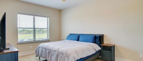 Een slaapkamer met een bed, een plafondventilator, een raam en een televisie.
