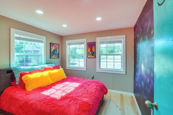 A bedroom with a large bed, multiple windows, and a door with a galaxy-themed wall. - 'galactikitty' - Quirky Cabin Near Lake Brownwood! (Brownwood)