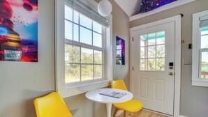 A room with a white door, two yellow chairs, a small white table, and a window with a view of trees. - 'galactikitty' - Quirky Cabin Near Lake Brownwood! (Brownwood)