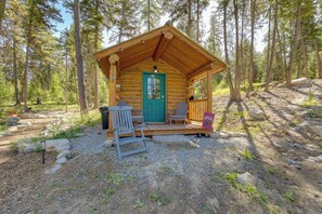 A rustic log cabin with a green door, a porch with two chairs, and a small table. - Mcgregor Lake Access: Cabin in Wooded Wilderness (Marion)