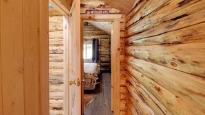 Interior de una cabaña de troncos con una cama, una puerta de madera y un letrero que dice 'Grizzly's Ave'.
