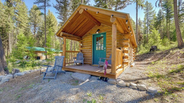 Una cabaña de troncos con un porche, una puerta verde y una pequeña terraza con sillas.
