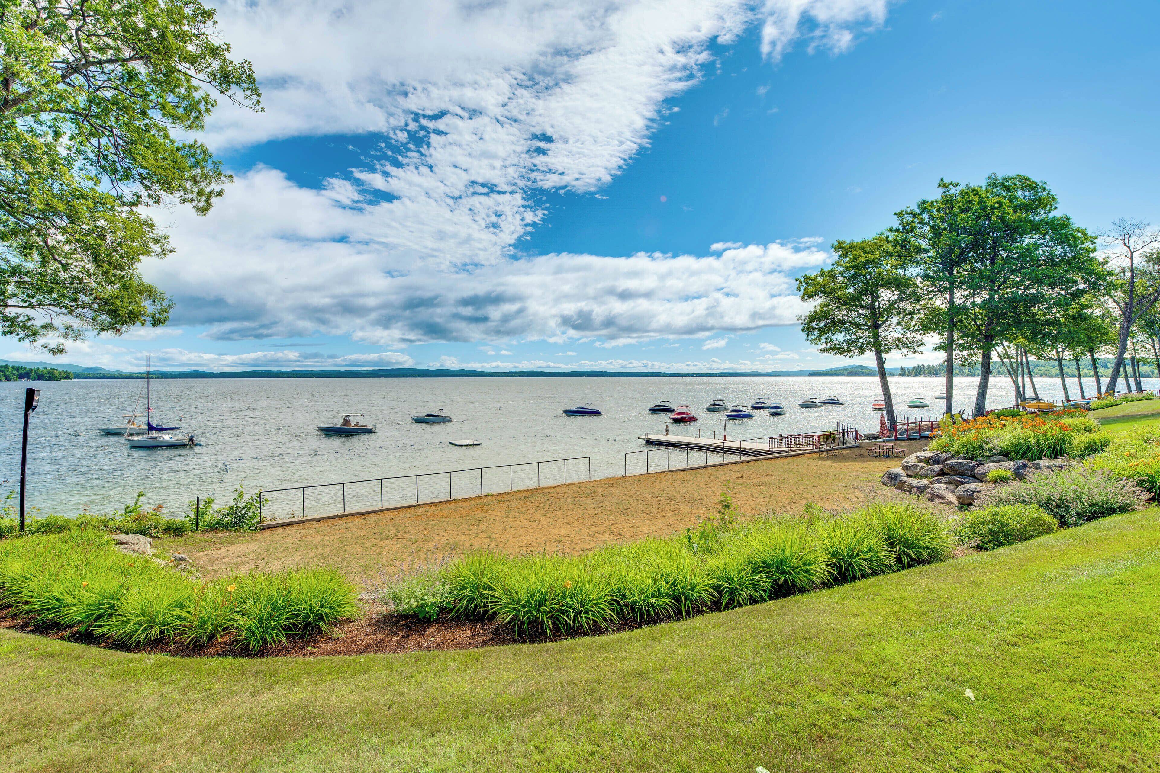 A lakeside view with boats, a grassy area, and trees.