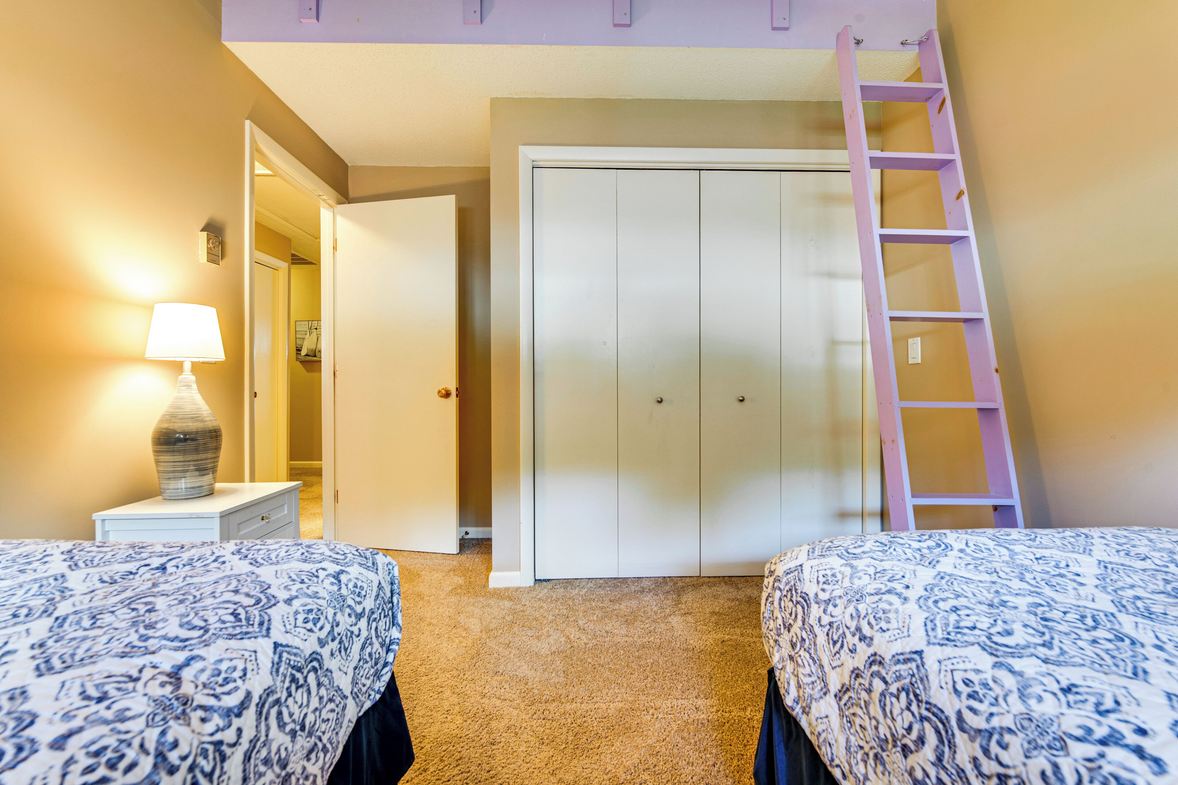 A bedroom with two beds, a nightstand with a lamp, a wardrobe, and a ladder.