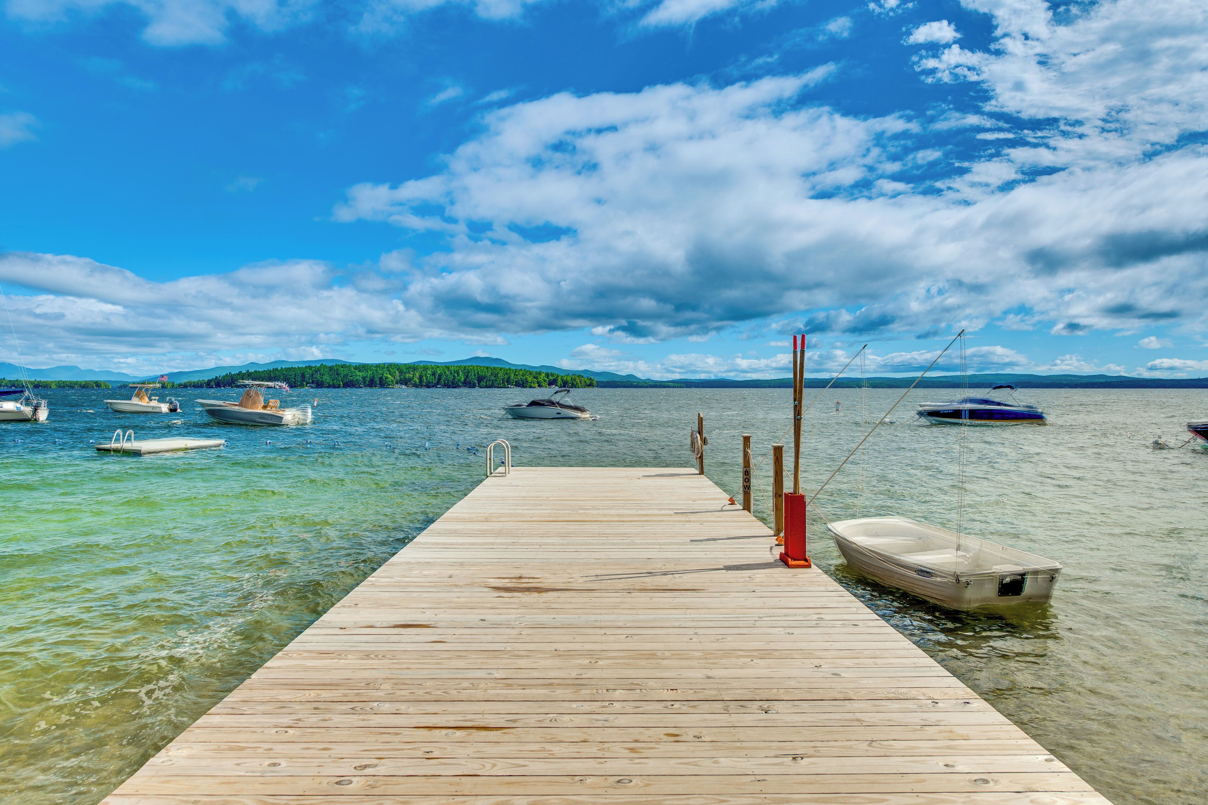 A wooden pier extending into a calm lake with several boats anchored nearby.