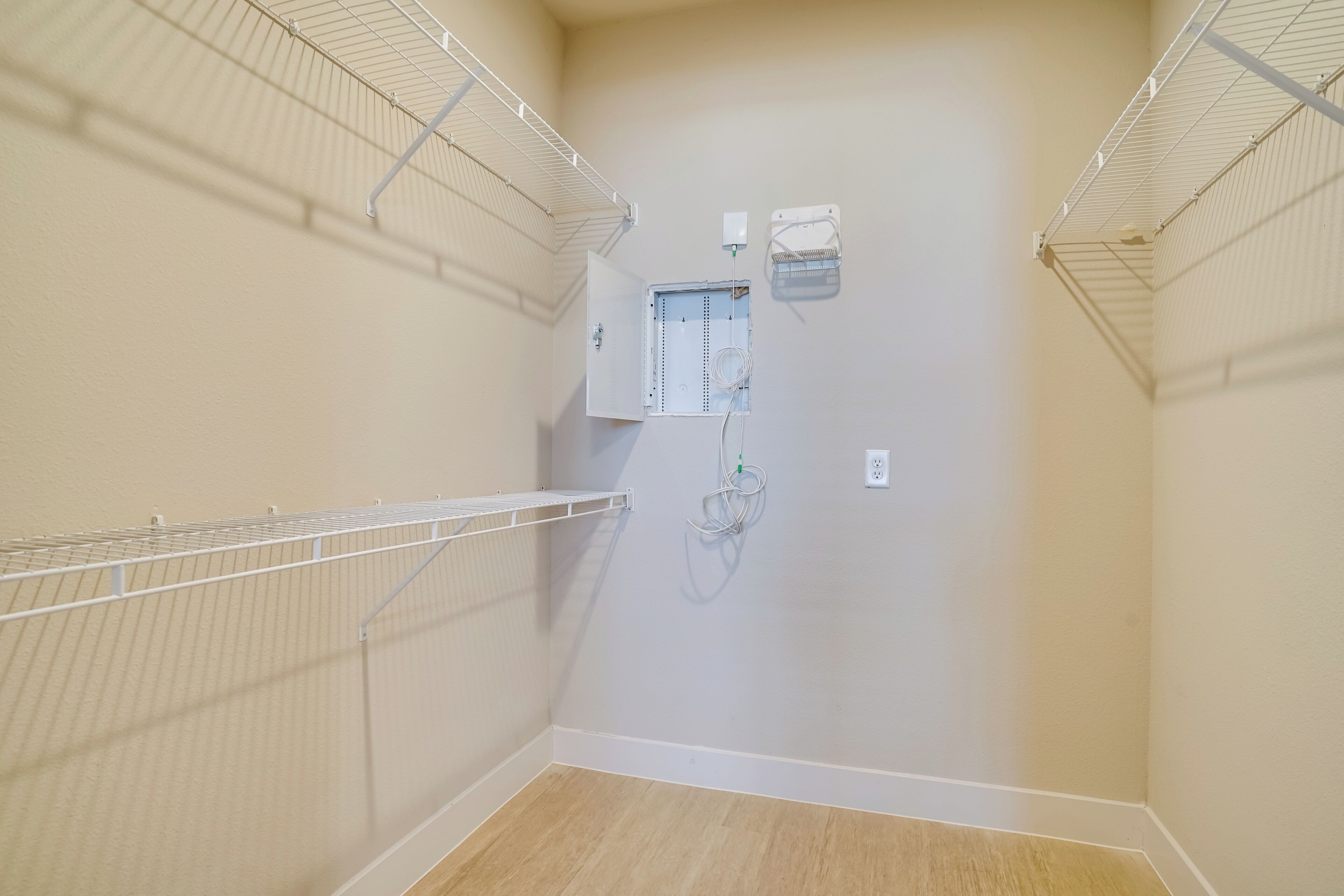 A room with a wooden floor, beige walls, and metal shelving units.