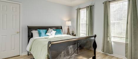 Un dormitorio con cama, mesita de noche, lámpara y ventana con cortinas.