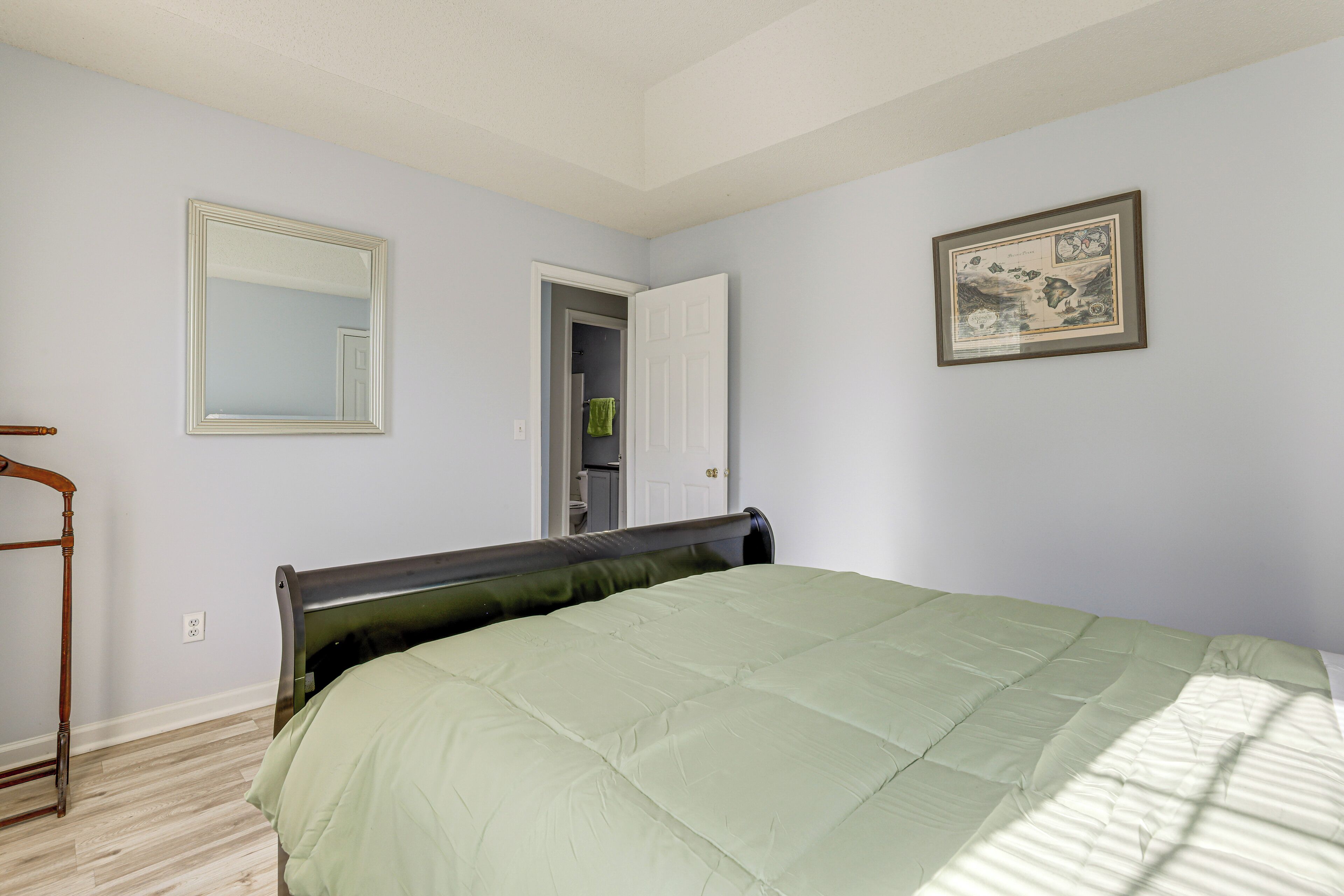 A bedroom with a bed, a mirror, a door, and a framed picture on the wall.