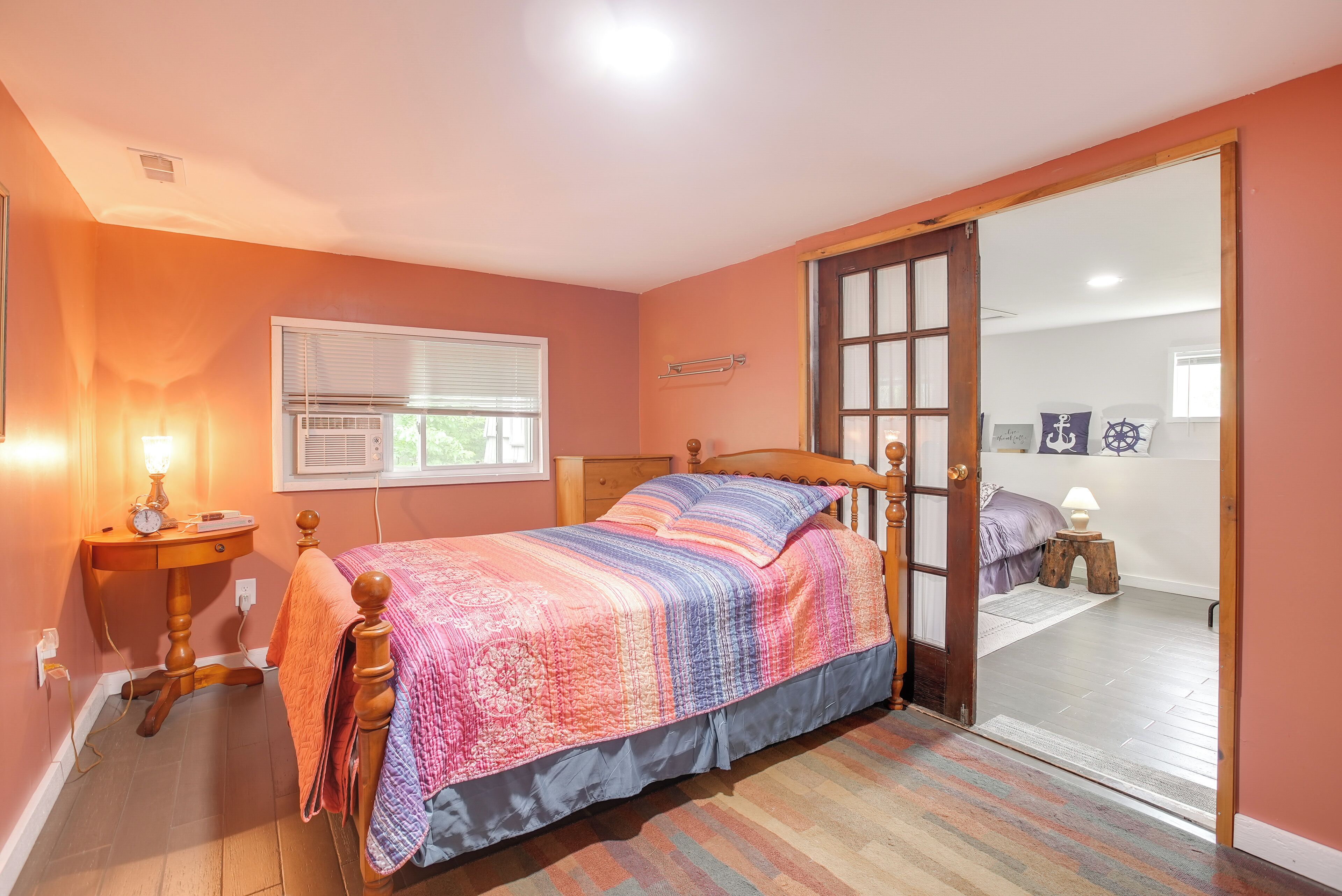A bedroom with a bed, bedside table, lamp, window, and a sliding door leading to another room.