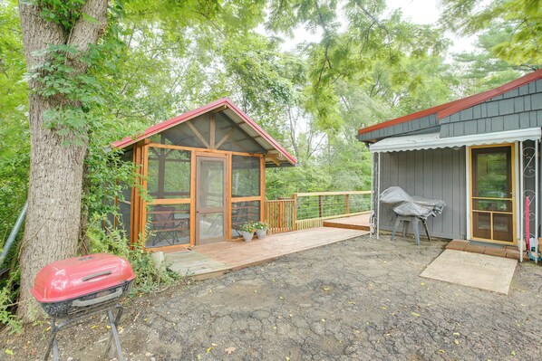 A cabin with a wooden deck, a covered outdoor seating area, and a barbecue grill.