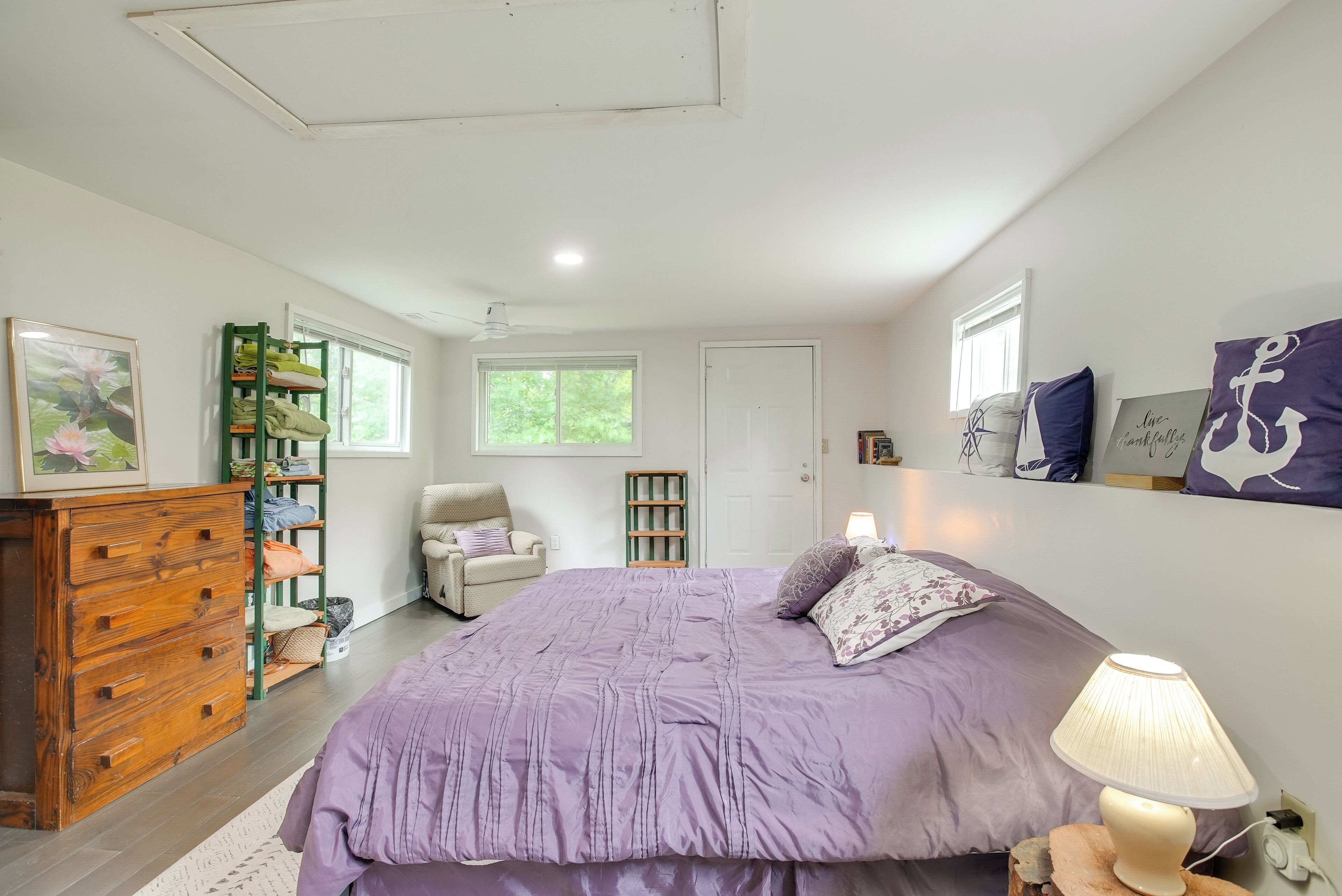 Une chambre à coucher avec un grand lit, une commode, une chaise, une lampe et une étagère où sont rangées des chaussures.