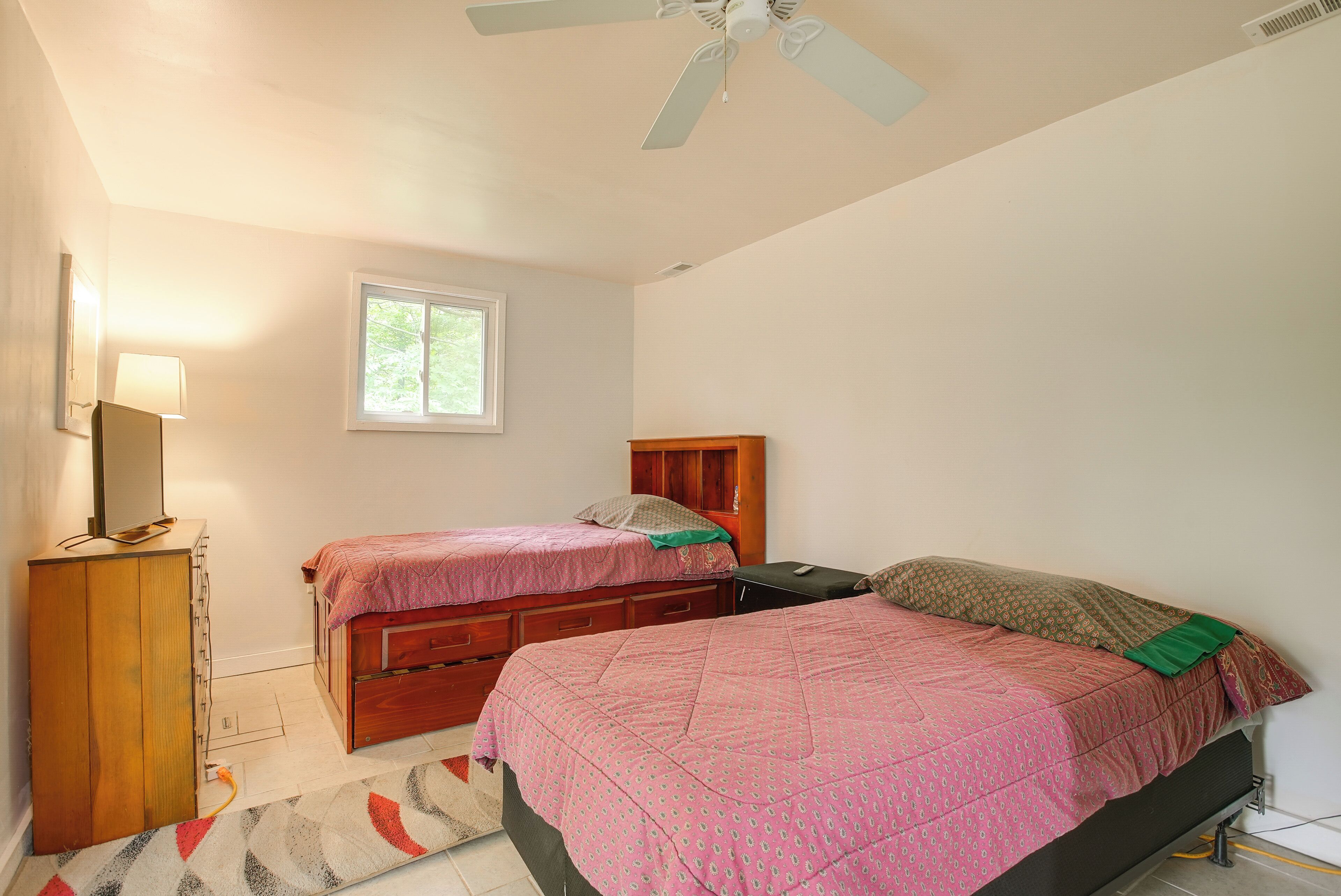 A bedroom with two beds, a dresser, a window, and a ceiling fan.