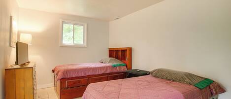A bedroom with two beds, a dresser, a window, and a ceiling fan.