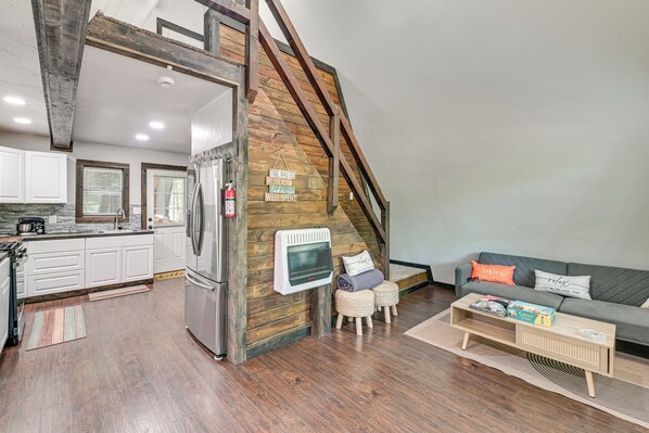 A loft-style living space with a kitchen, wooden beams, a fireplace, and a sofa with cushions. - 3 Mi to Lake Texoma: Gordonville Getaway! (Gordonville)