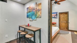 Una habitación pequeña con una mesa de madera, dos taburetes, un ventilador de techo y una puerta que da a otra habitación.
