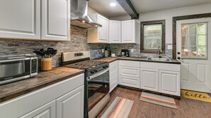 Una cocina moderna con armarios blancos, estufa de acero inoxidable, microondas integrado y salpicadero de piedra.