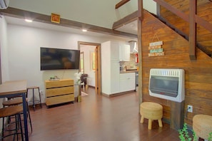 Una sala de estar moderna con televisor de pantalla plana, muebles de madera y una zona de cocina con armarios blancos.