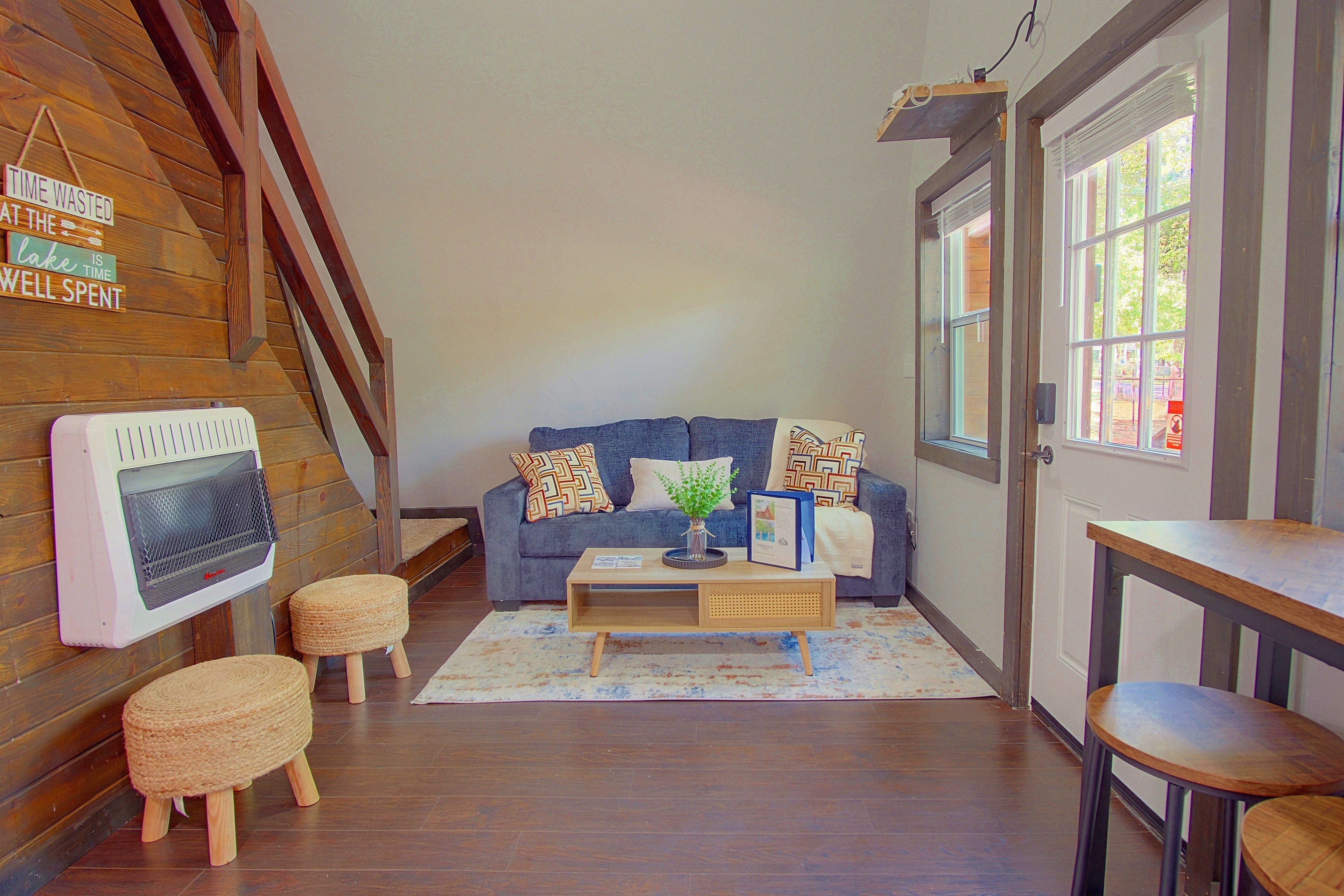 Una sala de estar acogedora con una escalera de madera, un sofá azul, una mesa de centro y una pequeña mesa de madera.