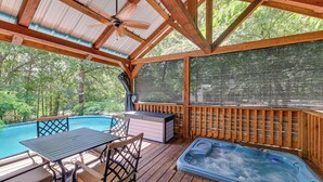 A wooden deck with a hot tub, a table with chairs, and a pool.