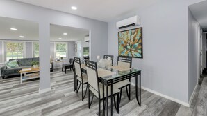 A modern dining area with a glass-top table and black chairs, a grey sofa, and a colorful abstract painting on the wall. - 12 Mi to Dtwn Lewes & Beach: Delaware Home w/ Deck (Georgetown)