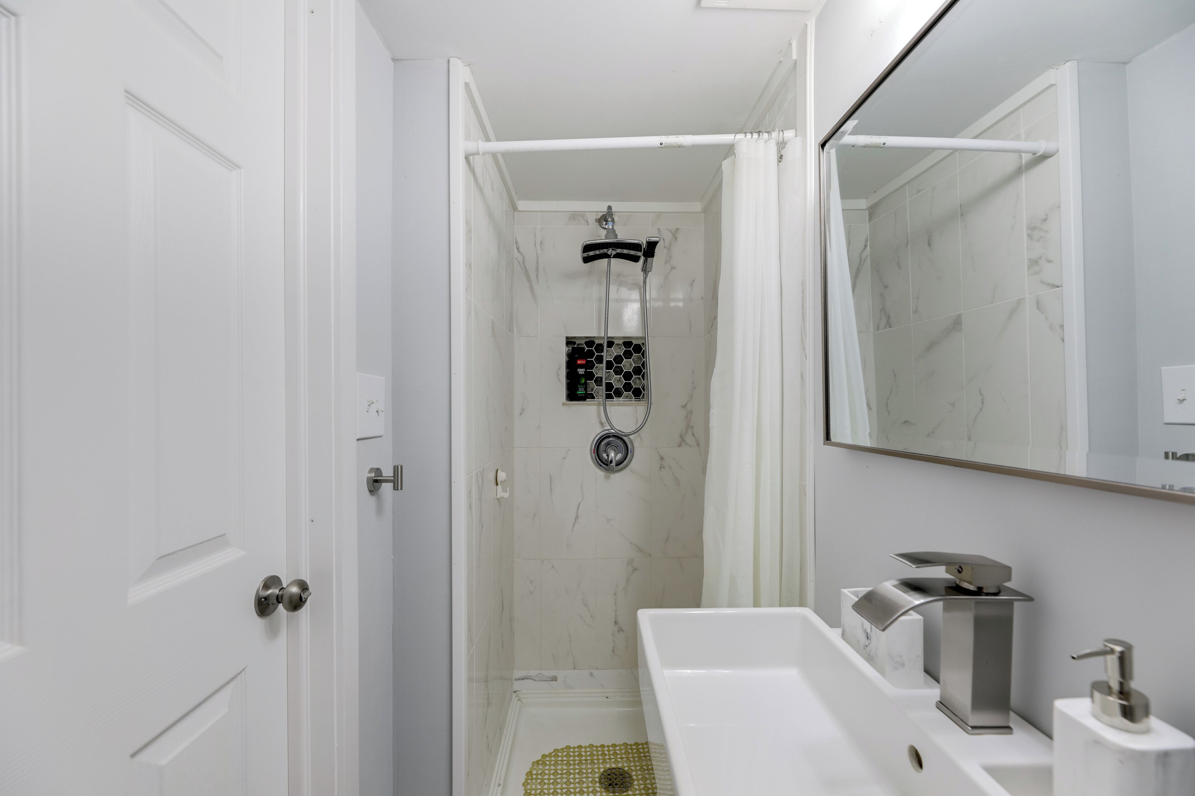 Une salle de bain moderne équipée d’une douche, d’un lavabo et d’un miroir.