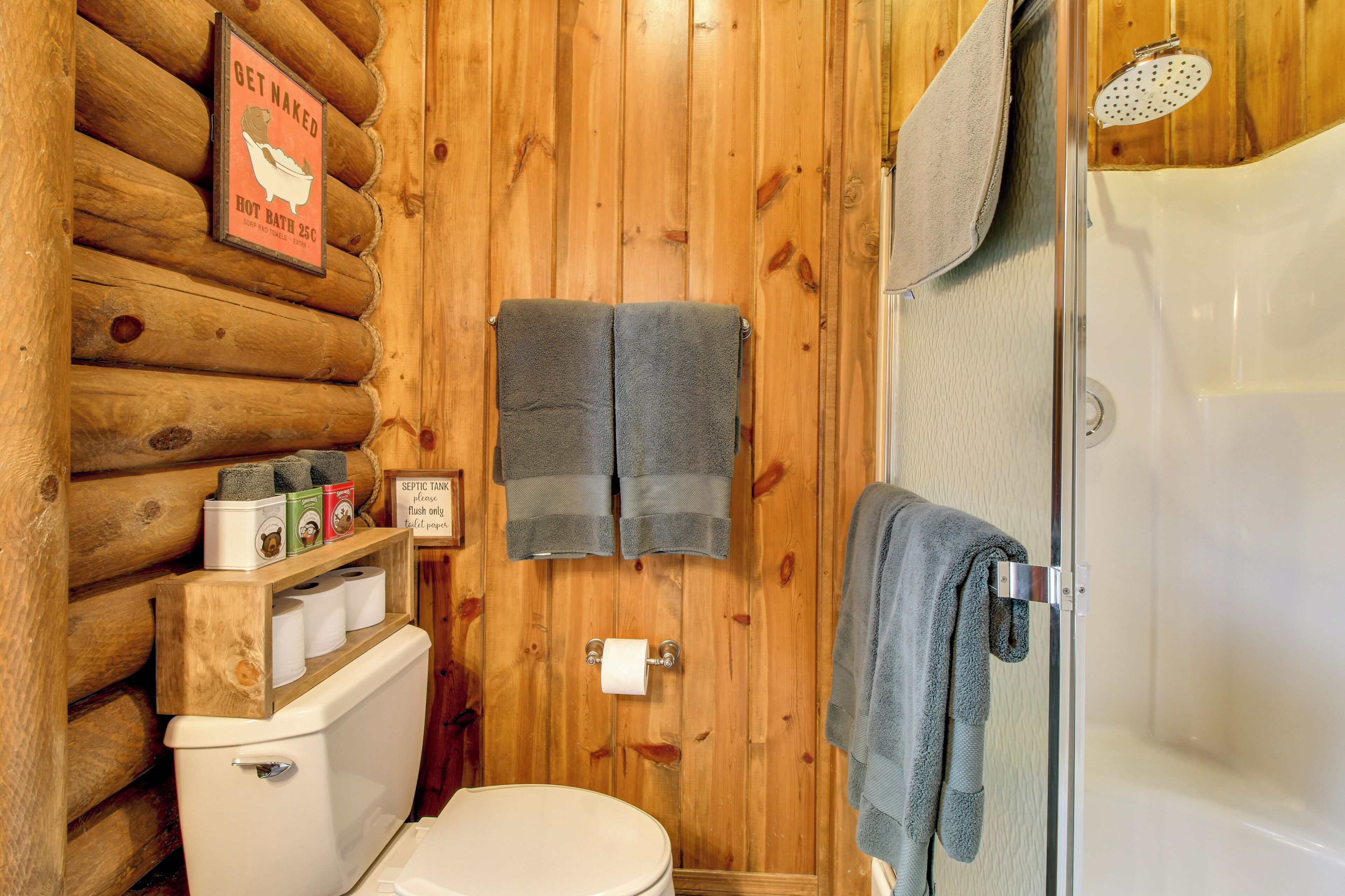 Une salle de bain rustique, aménagée dans une cabane en bois, comprenant des toilettes, une douche et un panneau indiquant qu’un bain chaud est disponible à une température de 25 degrés Celsius.