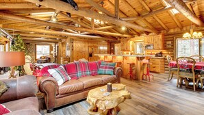 A cozy log cabin interior with a wooden ceiling, a leather sofa, a dining table with chairs, and a kitchen area. - Near Fishing & Hiking: Pinetop Log Cabin w/ Deck! (Pinetop)