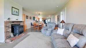 A spacious living room with a fireplace, a grey sofa, and a dining area in the background. - Community Boat Dock: Lake Memphremagog Condo! (Newport Center)