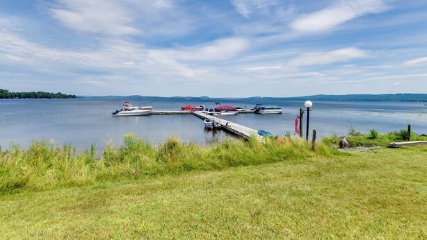 A lakeside dock with boats and a grassy shoreline. - Community Boat Dock: Lake Memphremagog Condo! (Newport Center)