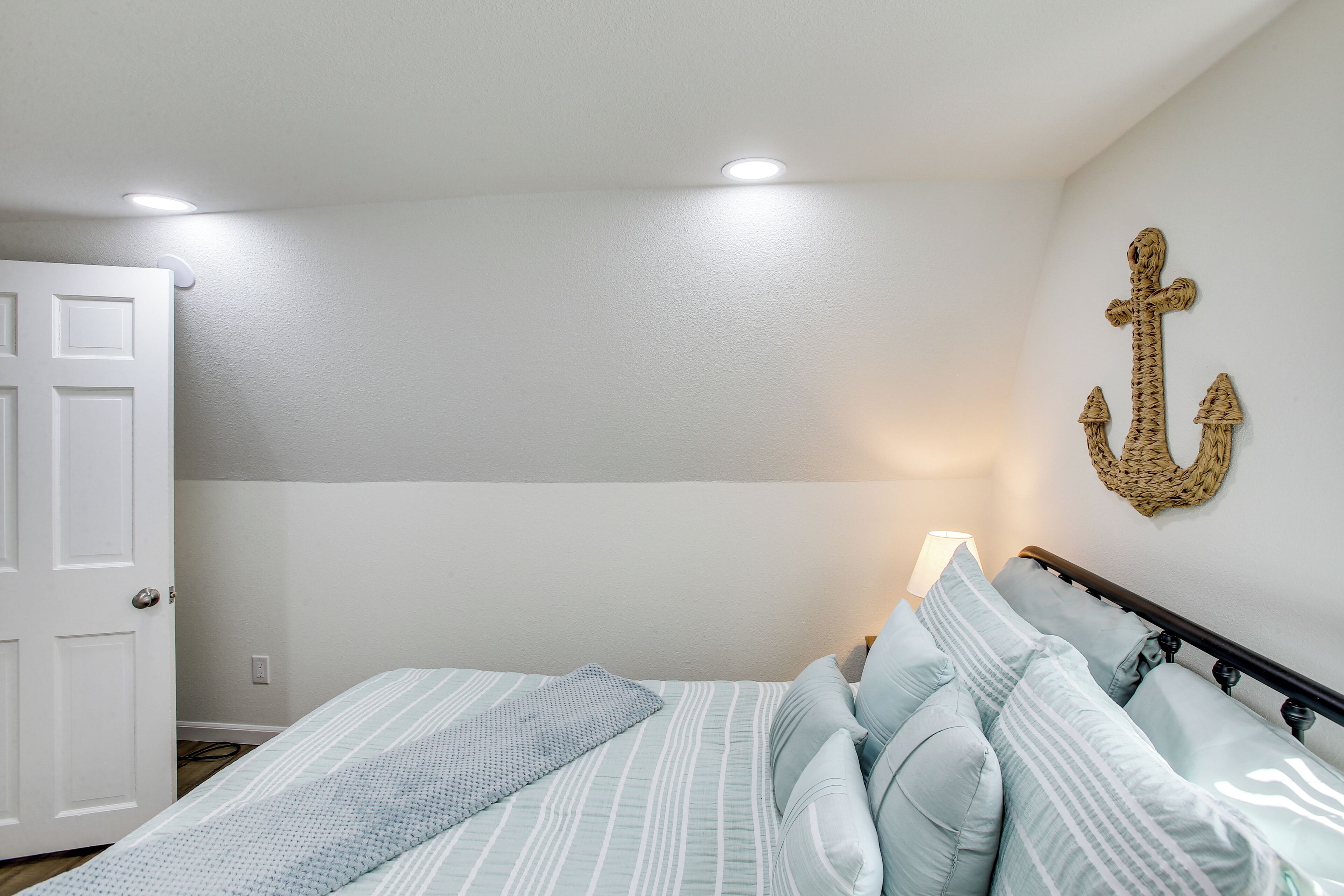 Une chambre à coucher avec un lit, un élément décoratif en forme d’ancre fixé au mur et une porte.