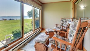Ein Zimmer mit großem Fenster, das einen Blick auf eine grüne Fläche und Wasser bietet, mit Holzmöbeln und einem fest installierten Heizkörper.
