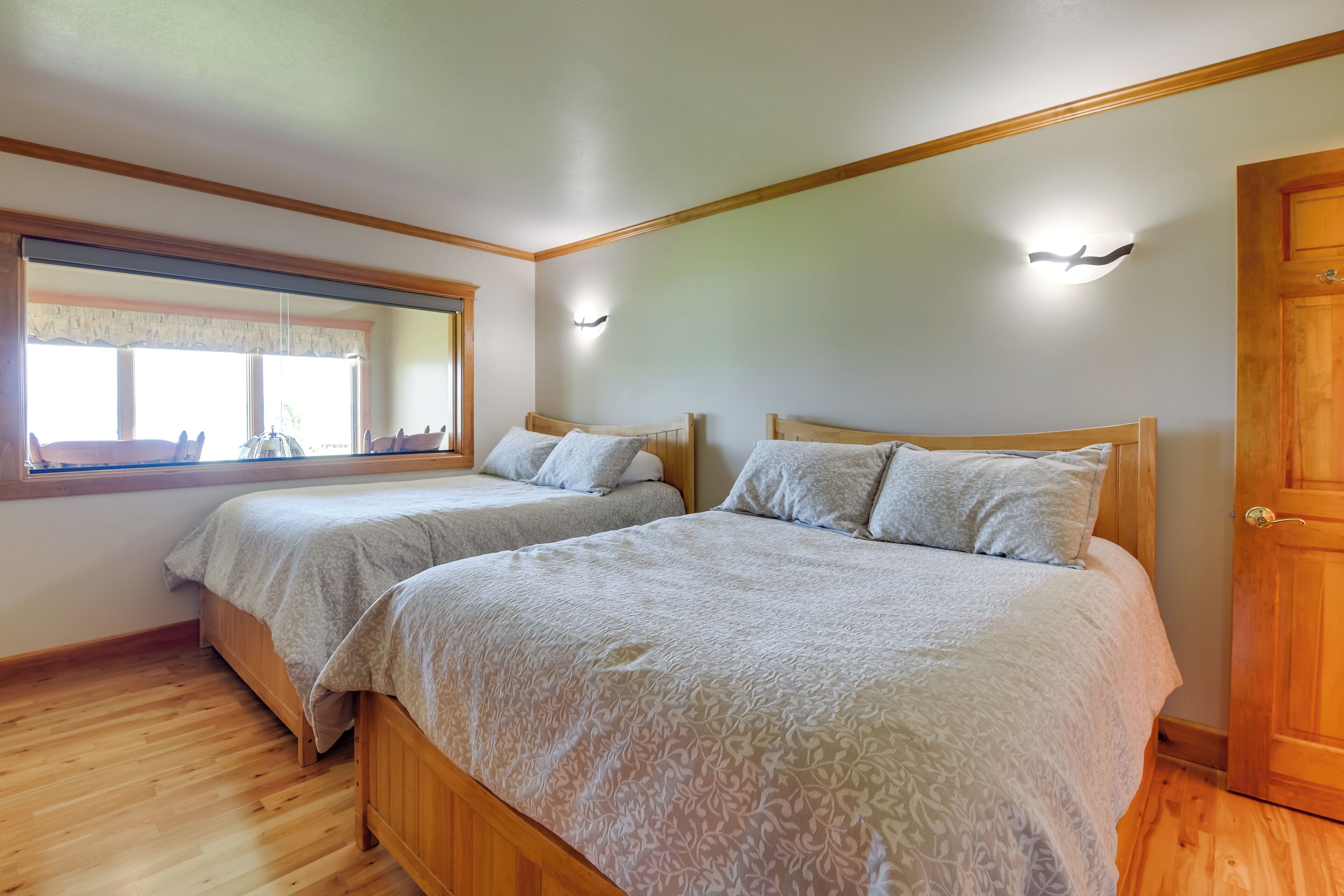 A bedroom with two beds, wooden flooring, a large window, and a mirror.