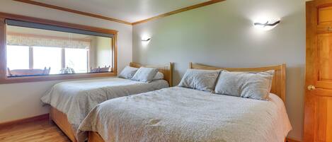 A bedroom with two beds, wooden flooring, a large window, and a mirror.