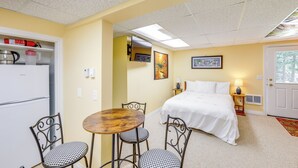 A hotel room with a bed, a small table with chairs, a refrigerator, and a door with a window. - Crystal Lake Retreat Studio: Walk to Happy's Inn! (Libby)