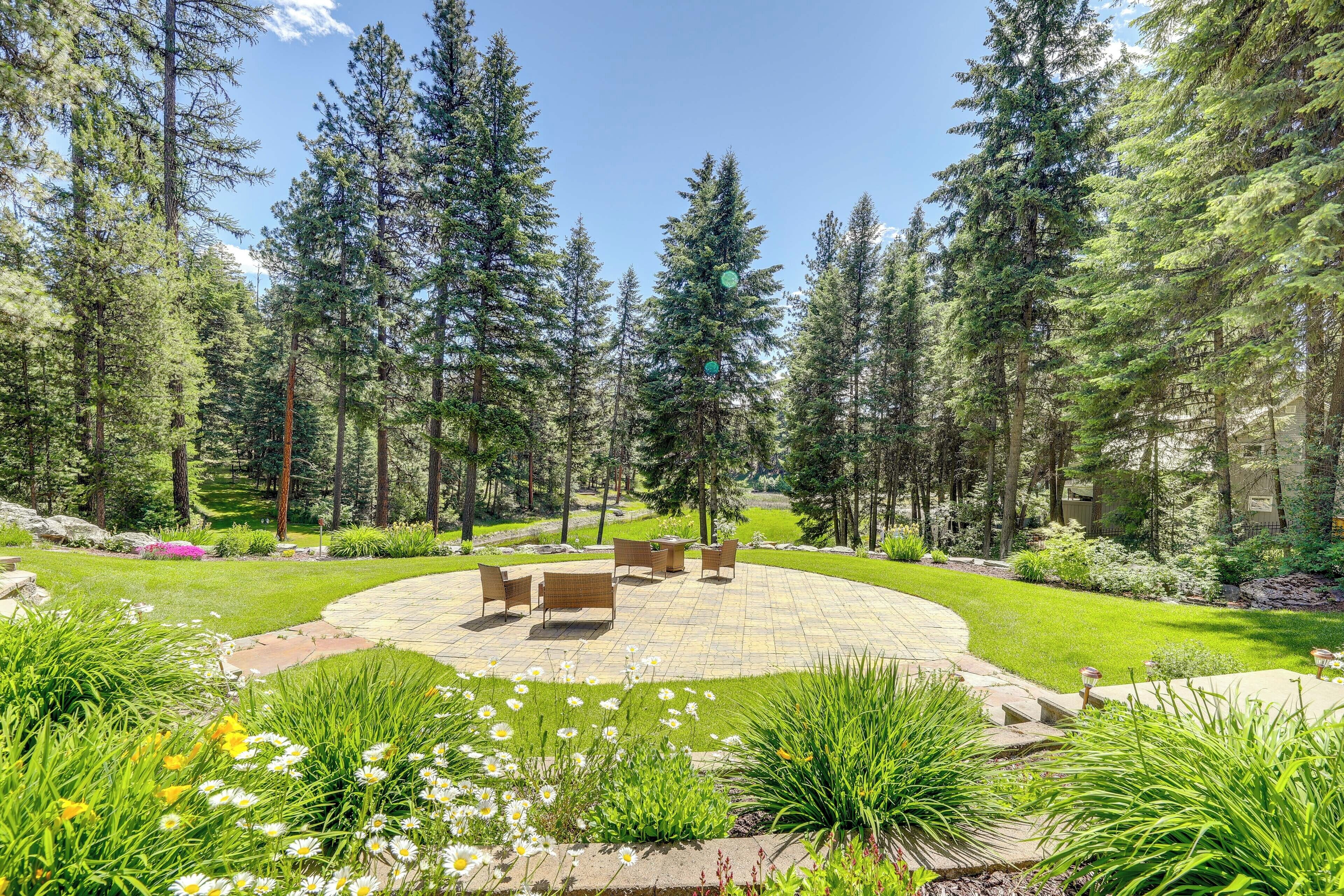 A patio area with outdoor furniture, surrounded by a well-maintained garden and tall trees.