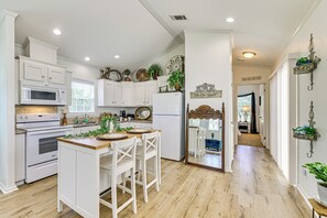 Cocina con armarios blancos, una isla central con taburetes, microondas, horno y refrigerador.