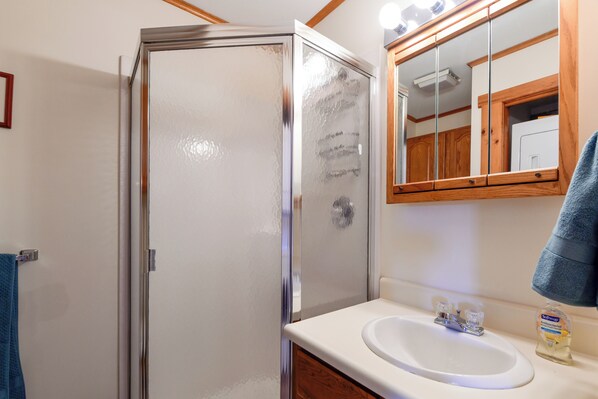 Un baño con cabina de ducha de vidrio, un lavabo blanco y un espejo sobre él.