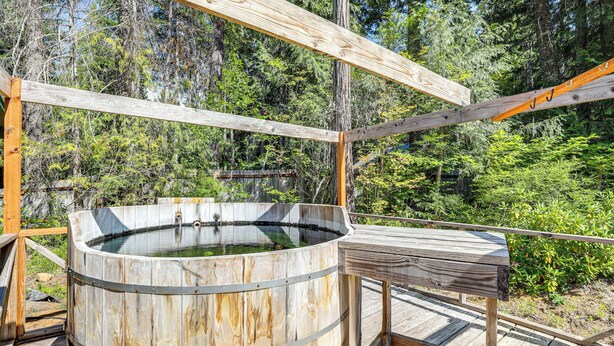 Eine Holzterrasse mit Whirlpool, umgeben von einem Holzzaun und dichtem Wald.