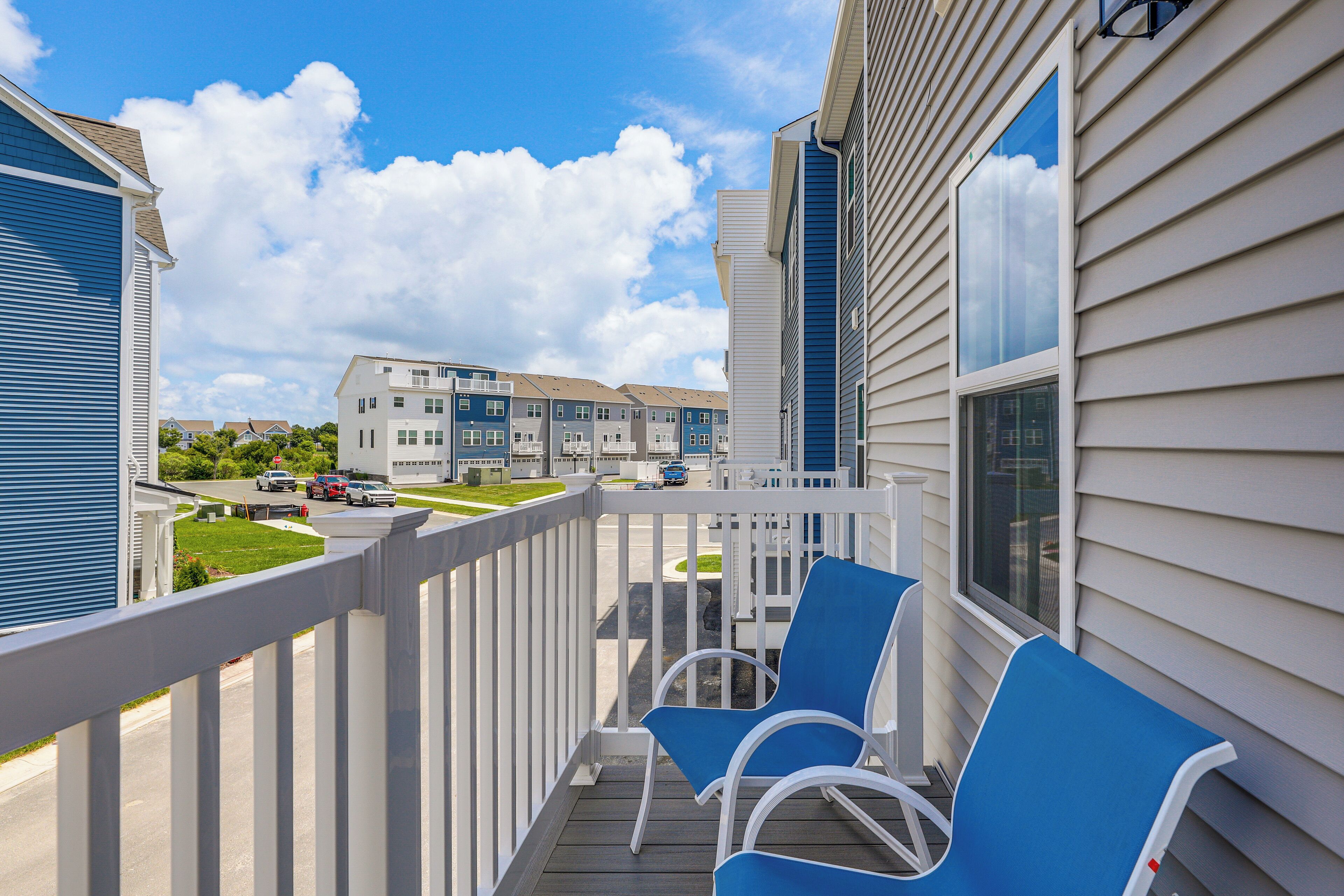 A balcony with blue chairs, a white railing, and a view of neighboring buildings.