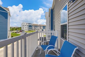 A balcony with blue chairs, a white railing, and a view of neighboring buildings.