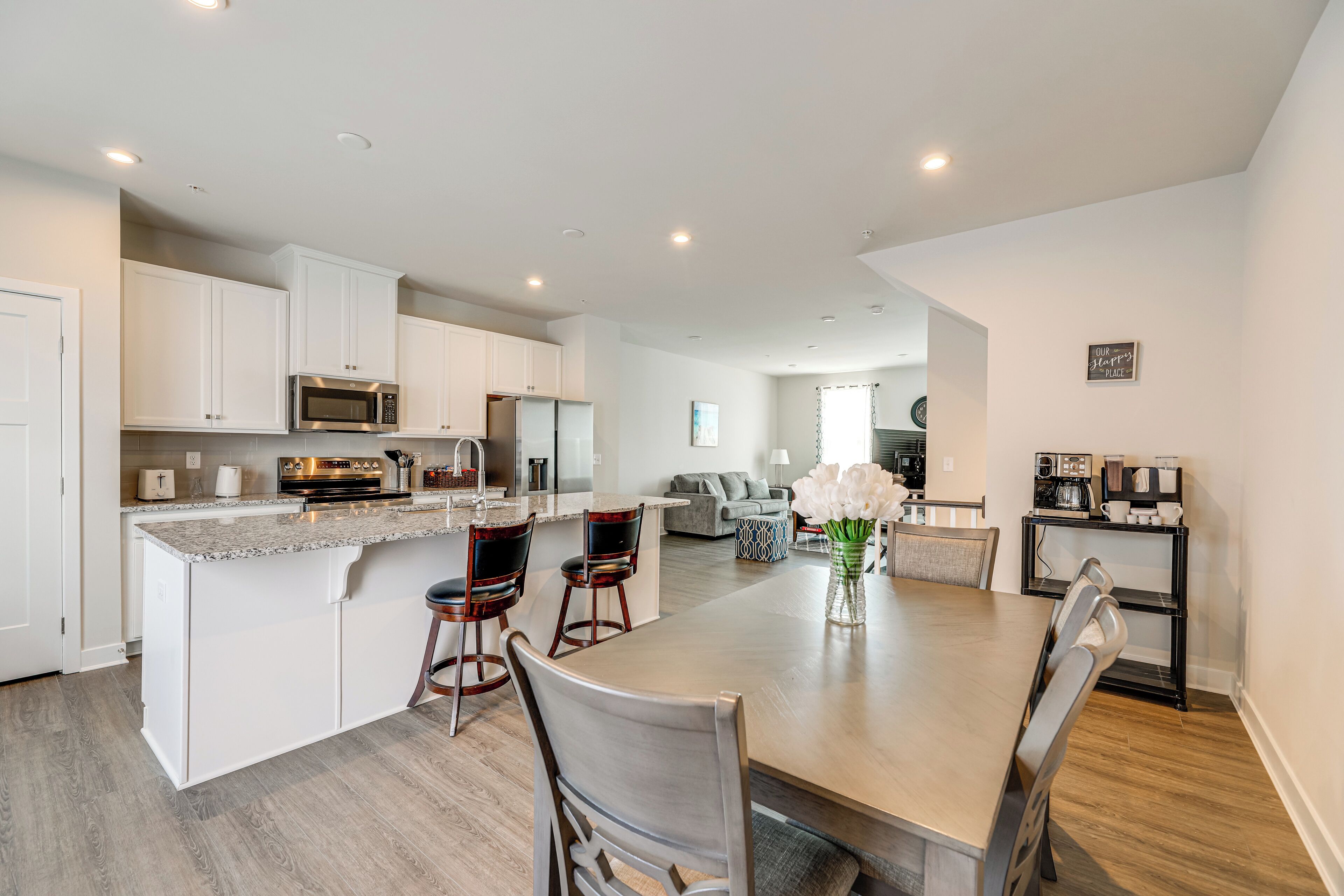 A modern kitchen with white cabinets, a central island with bar stools, and a dining area with a large table and chairs.