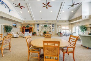 A spacious living area with a round wooden table, several chairs, ceiling fans, and a large plant.