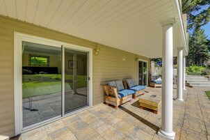 A covered patio with a sliding glass door leading to a backyard, a wooden bench, and a cushioned seating area.