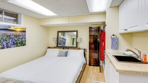 Un dormitorio con cama, una kitchenette pequeña, un espejo y una ventana con vistas a flores.