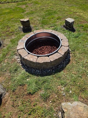 Un hogar circular de piedra con un recipiente metálico en el centro, rodeado por un anillo de piedra y una base de grava.