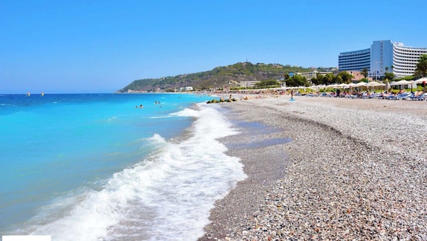 A pebble beach with clear blue waters, a few people, and a building in the background. - Villa Lilienne - Tranquil Escape With Private Garden Balcony (Rhodes)